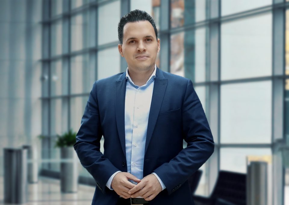 Mann in formeller Kleidung steht in modernem Gebäude mit großen Fenstern.